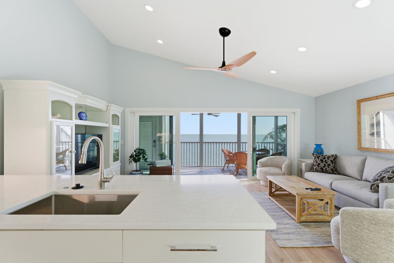 A spacious living area with a kitchen, a balcony with a view of the ocean, and a ceiling fan.