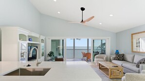 Un amplio salón con cocina, un balcón con vistas al océano y un ventilador de techo.