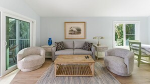 Un salón amplio con un sofá gris, dos sillones, una mesa de centro de madera y un cuadro en la pared.