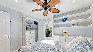 A bedroom with a bed, a ceiling fan, a wardrobe, and a window with a view of greenery. - Captiva Hide-A-Way 1A (Captiva)