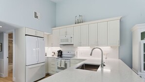 A modern kitchen with white cabinetry, a stainless steel sink, and a built-in oven. - Captiva Hide-A-Way 1A (Captiva)