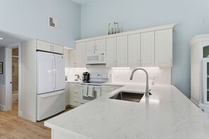 A modern kitchen with white cabinetry, a stainless steel sink, and a built-in oven. - Captiva Hide-A-Way 1A (Captiva)