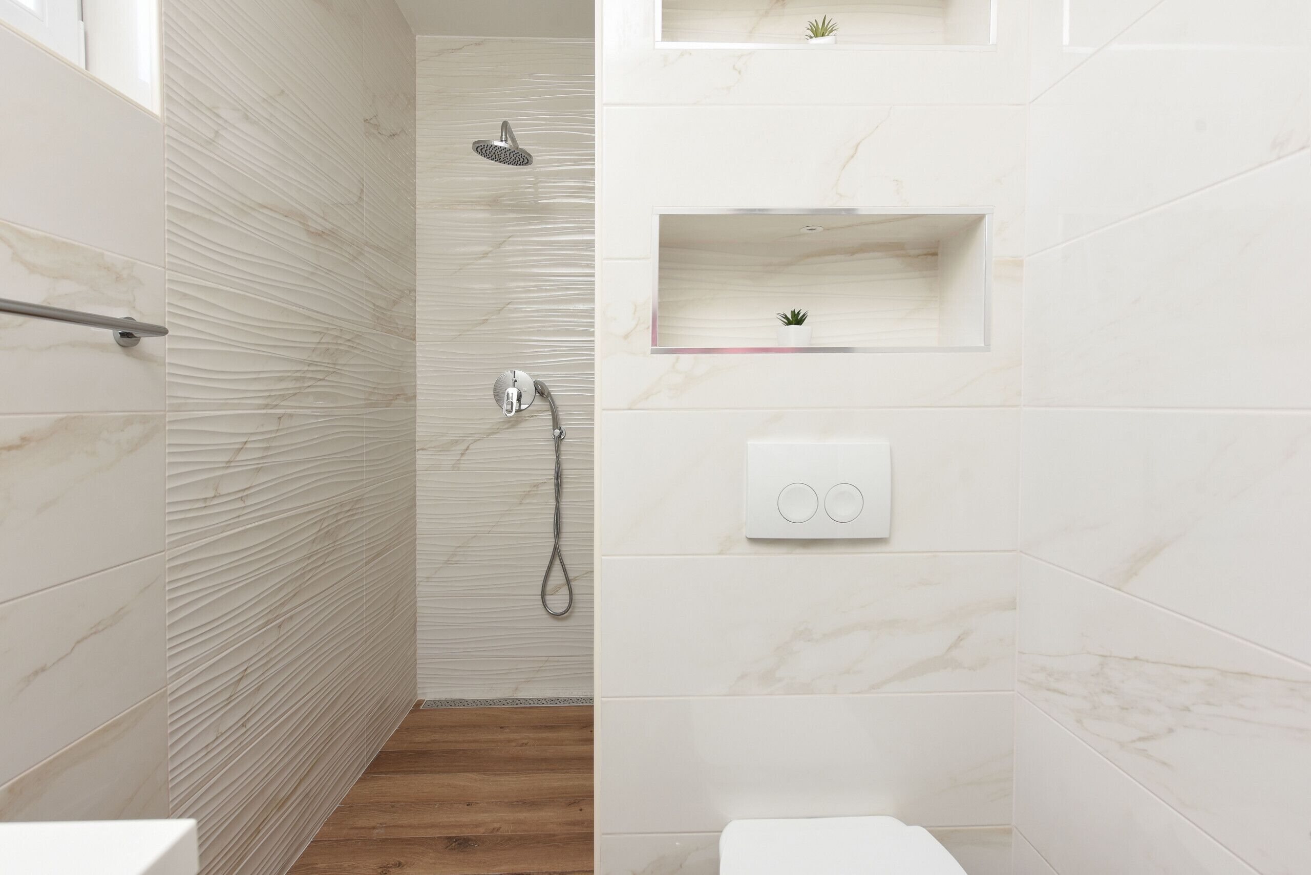 Un baño moderno con ducha, inodoro y una pequeña estantería con una planta.