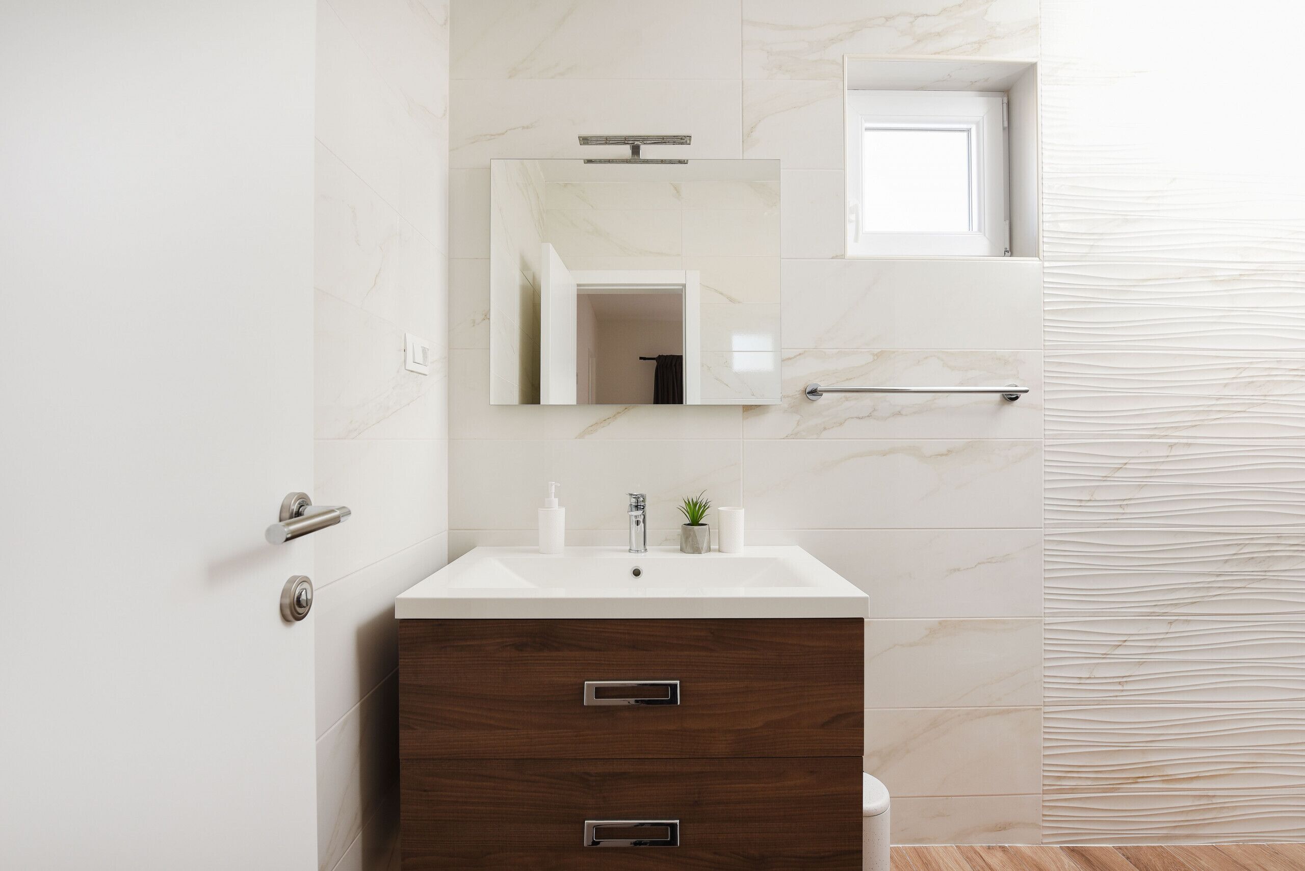 A modern bathroom with a marble sink, a wooden vanity, a mirror, and a towel rack.
