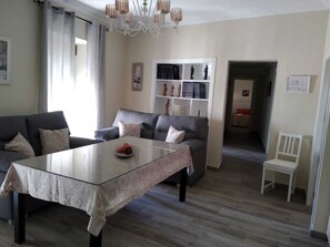 Una sala de estar moderna con una mesa de centro de vidrio, sofás grises y una estantería blanca.