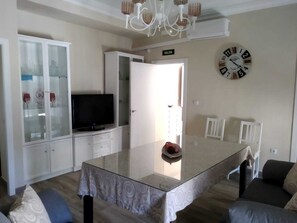 Una sala de estar moderna con una mesa de comedor de vidrio, un televisor de pantalla plana y un reloj en la pared.
