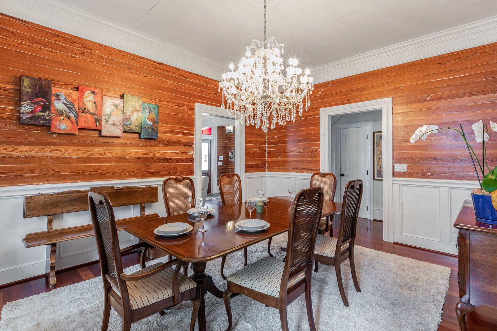 Een eetkamer met houten lambrisering, een kroonluchter en kunstwerken aan de muur.
