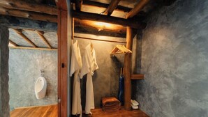 Une salle de bain rustique avec des poutres en bois, un banc en bois, un porte-vêtements suspendu et un urinoir blanc.