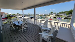 A covered outdoor deck with a table and chairs, overlooking a marina with boats and houses in the background. - Stunning waterfront home, beach, pools, pet friendly! (Long Neck)