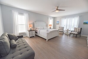 A bedroom with a bed, two chairs, a nightstand, a dresser, and a ceiling fan.