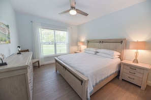 A bedroom with a bed, bedside tables, a desk, a ceiling fan, and a window with curtains.