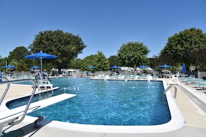 A rectangular swimming pool with multiple lanes, surrounded by lounge chairs and blue umbrellas.