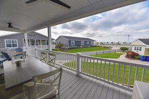 A covered outdoor area with a table and chairs, a white railing, and a view of a residential neighborhood.