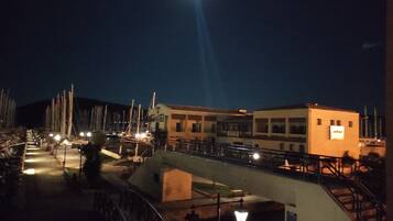 Vista nocturna de un puerto deportivo con barcos, un puente y edificios con letreros iluminados.