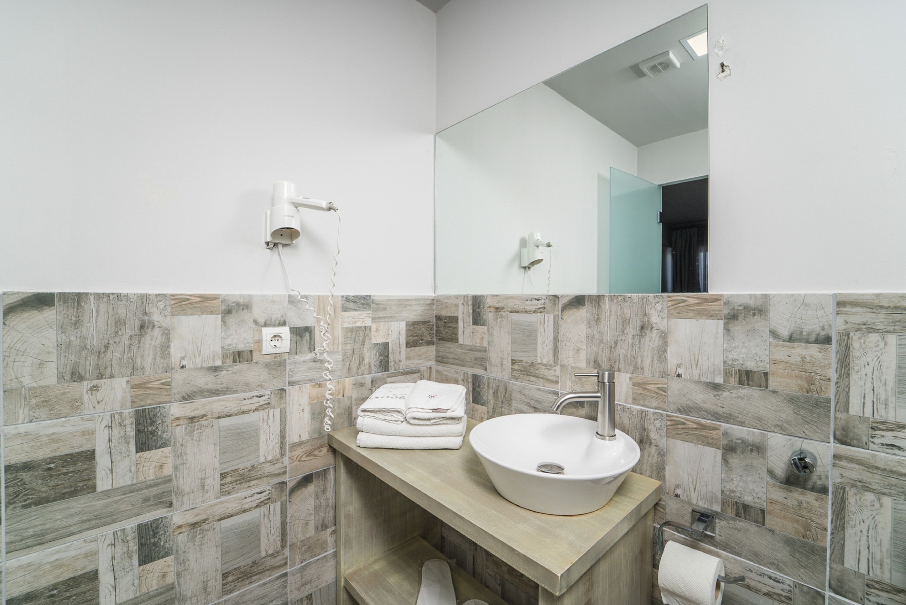 Un baño con tocador de madera, lavabo blanco y espejo.