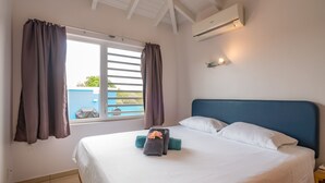 A bedroom with a large bed, a window with curtains, an air conditioning unit, and a nightstand. - Villa Despacito (Sint Willibrordus)