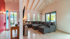 A spacious living room with a large sectional sofa, a wooden coffee table, and a view of the outdoors through large windows. - Villa Despacito (Sint Willibrordus)
