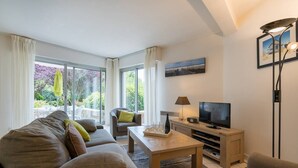 A modern living room with a sofa, armchairs, a coffee table, a TV, and a dining area with a table and chairs. - Carnac - 3-room apartment - 69m² - Wifi (CARNAC)