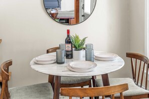 Una mesa redonda para comer con platos blancos, una botella de vino y copas decorativas.