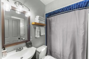 Un baño con lavamanos, espejo, toallero y cortina de ducha.