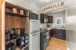 A modern kitchen with a Galane refrigerator, a microwave, a coffee maker, and a toaster. There is a wooden shelf with containers and a sign that reads 'LEADVILLE ELEV. 10.152'. - Pine Street Retreat | 1BR Hot Tub Home, Dog Door, Walk to Main St | Leadville (Leadville)
