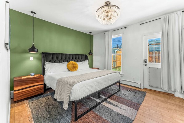 Un dormitorio con cama, mesitas de noche, una araña de cristal y vistas a través de una puerta, además de una pared verde.