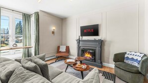 A living room with a sofa, armchair, fireplace, and a TV displaying 'NETFLIX'. - Pine Street Retreat | 1BR Hot Tub Home, Dog Door, Walk to Main St | Leadville (Leadville)