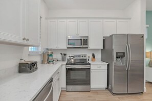 A modern kitchen with white cabinets, stainless steel appliances including a microwave, stove, and refrigerator, and a marble countertop. - Disney near! 3BR Cottage w Patio & Free Parking (Kissimmee)