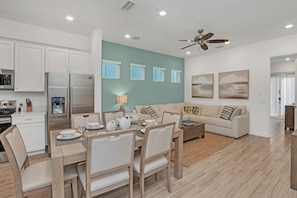 A modern kitchen with white cabinets, a stainless steel refrigerator, and a dining area with a wooden table and chairs.