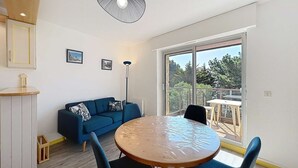 A room with a round wooden table, blue chairs, a blue sofa, and a large window with a view of trees. - Quiberon - 2rooms + duplex - 38m² - near beach (QUIBERON)