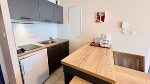 Een compacte keuken met een inbouwfornuis, spoelbak en een koffiezetapparaat op een houten tafel.