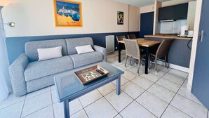 Een gezellige, compacte leefruimte met een bank, een salontafel, een eettafel met stoelen en een kitchenette.