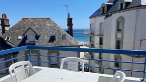 Een balkon met een tafel en stoelen, met uitzicht op een kustgebied met gebouwen en de zee.