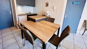 Een kleine keuken met een eettafel en stoelen, een koffieapparaat en een deur met de tekst 'Belle Ile'.