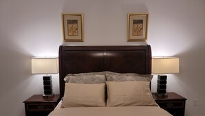 Un lit avec une tête de lit, deux tables de chevet avec des lampes et deux tableaux encadrés accrochés au mur.