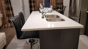 Une cuisine moderne dotée d’un îlot central, d’appareils électroménagers en acier inoxydable et d’un coin repas avec une chaise noire.