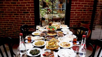 Mesa dispuesta con diversos platos y bebidas, rodeada de paredes de ladrillo y una ventana con plantas.