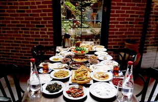 Mesa dispuesta con diversos platos y bebidas, rodeada de paredes de ladrillo y una ventana con plantas.