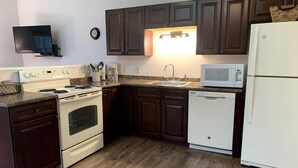 A kitchen with dark wooden cabinets, a white stove, a microwave, and a dishwasher. - Western Mountain Townhouse (Southwest Harbor)