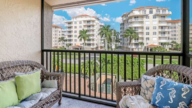 A balcony with wicker furniture and a view of a multi-story residential building. - Paradise - quiet, clean, upgraded condo; walk to beach (Marco Island)