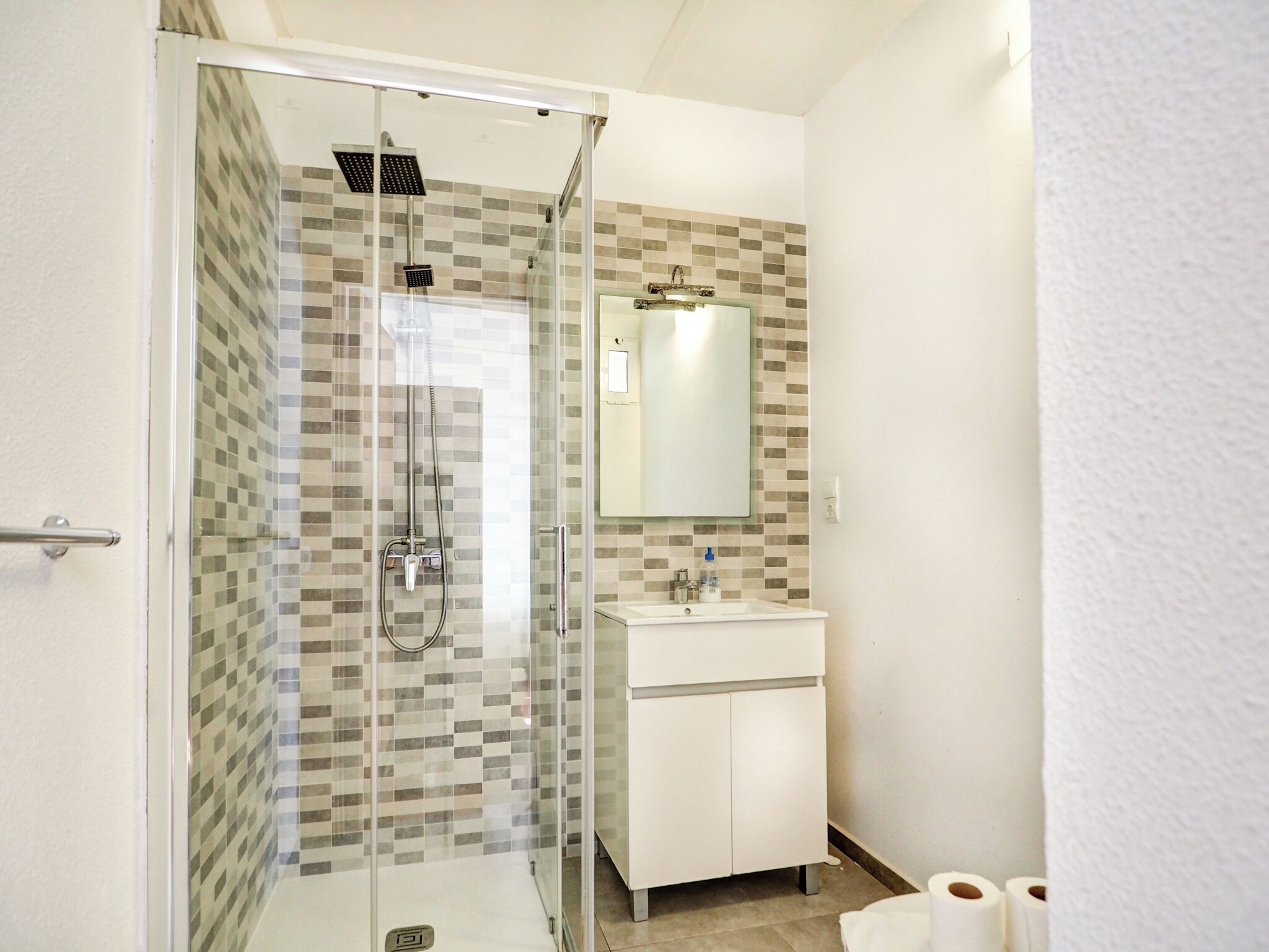 Un bagno moderno con doccia vetrata, lavandino bianco e specchio sopra.