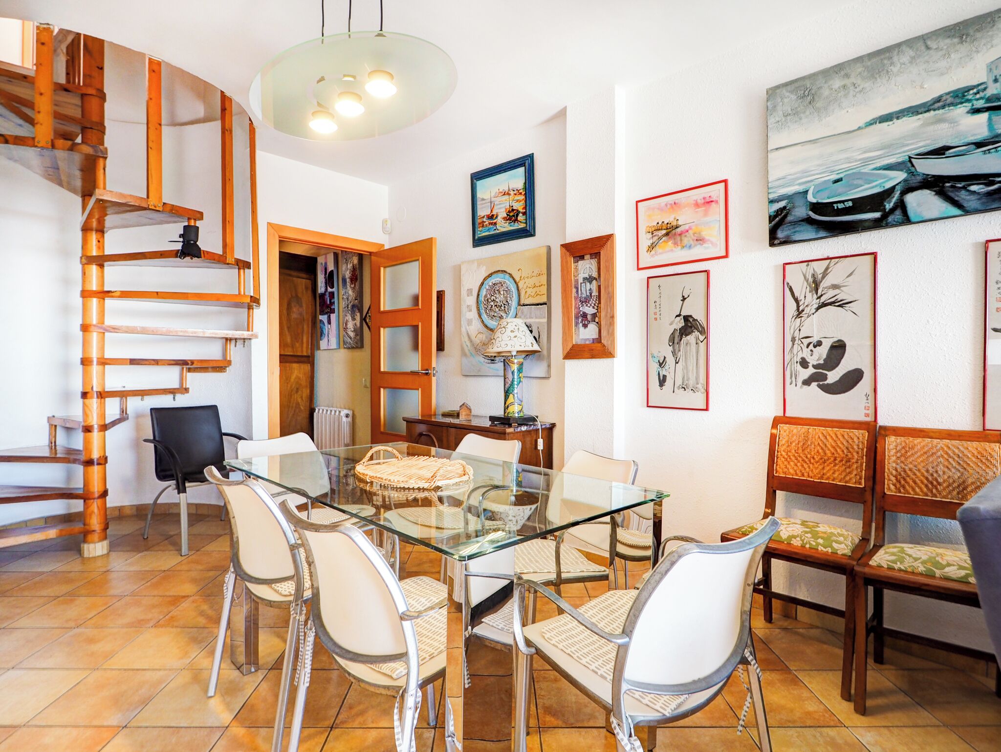 A dining area with a glass table, white chairs, and a wooden staircase.