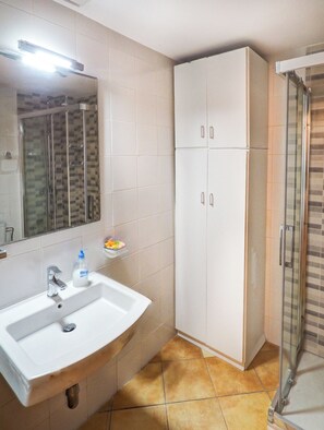 Une salle de bain avec un lavabo blanc, un miroir, une cabine de douche et un meuble de rangement.