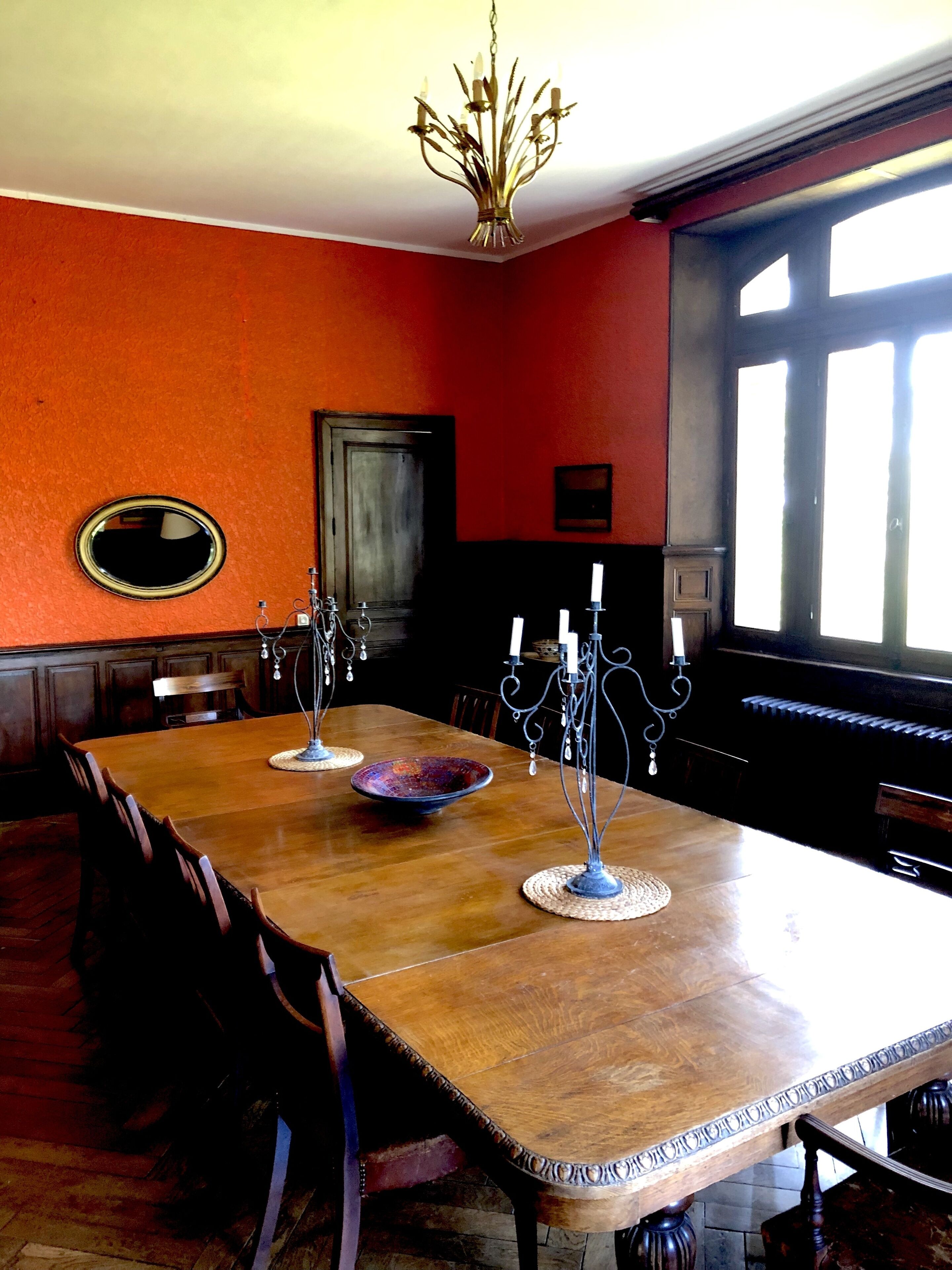A dining room with a wooden table, chairs, a chandelier, and a piano.