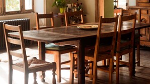 Un espace repas avec une table et des chaises en bois, un luminaire suspendu et une vue sur l’extérieur grâce à une grande fenêtre.