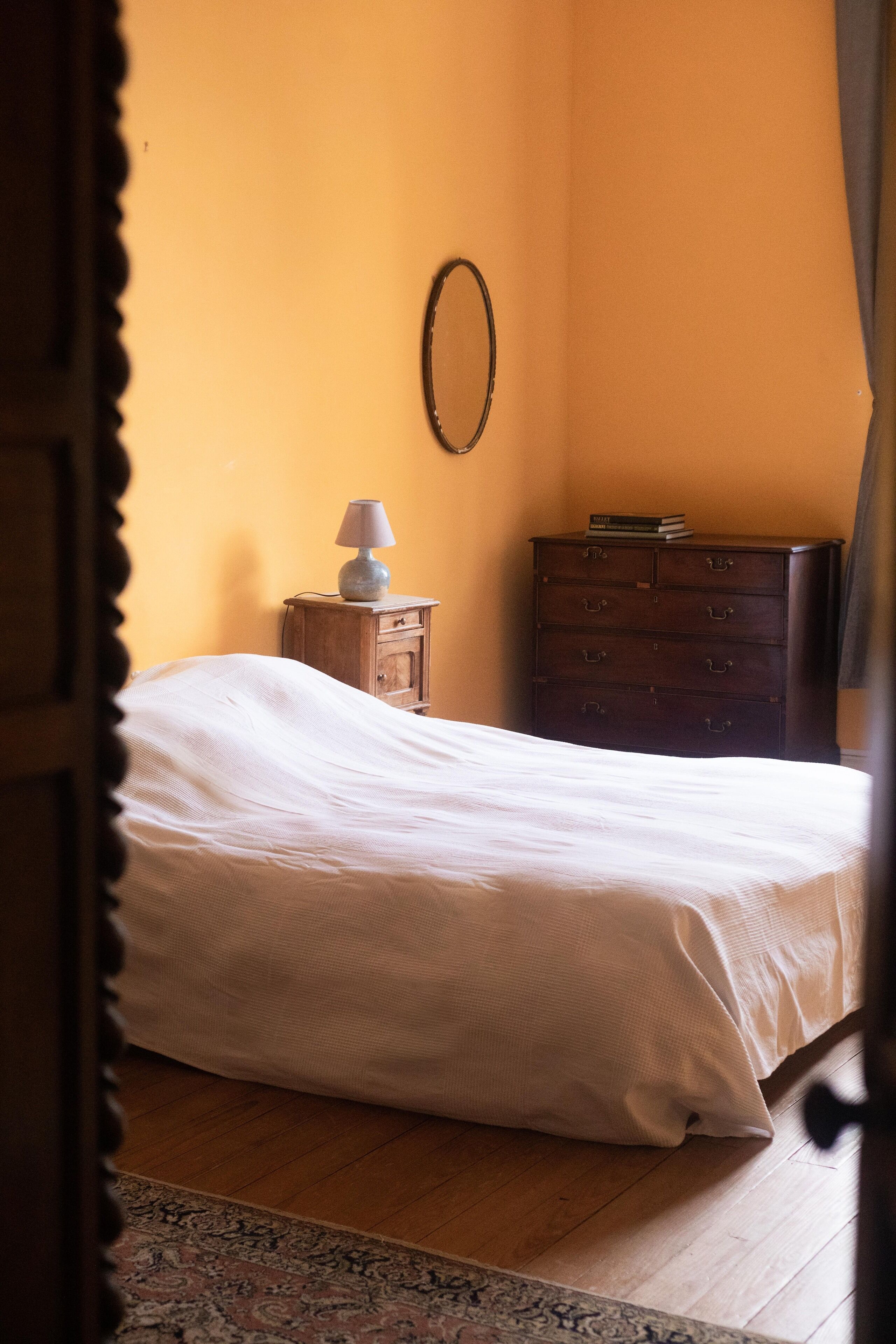 Un dormitorio con cama, cómoda, lámpara y espejo en la pared.