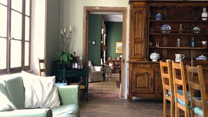 Un salon chaleureux avec un canapé vert, une table à manger en bois avec des chaises et un buffet en bois contenant de la vaisselle.