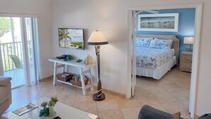 Un dormitorio con una cama, una mesita de noche, una lámpara, un escritorio con una silla, una ventana y un cuadro en la pared.