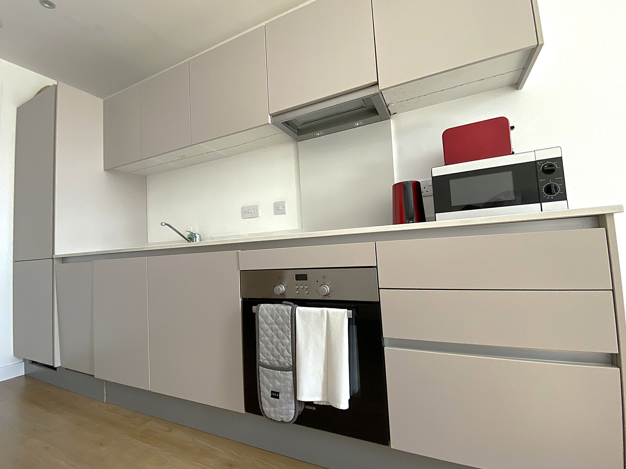 A modern kitchen with a built-in oven, microwave, and a red appliance on the countertop.