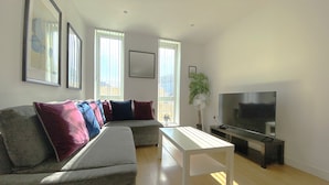 A modern living room with a grey sofa, a white coffee table, and a flat-screen TV.
